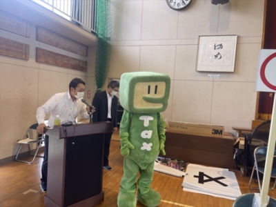 司会中の田村運営専務と国税庁マスコットキャラクター「イータ君」 司会中の田村運営専務と国税庁マスコットキャラクター「イータ君」